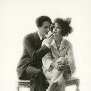 Androgynous man in suit applying lipstick to lips of girl in pyjamas (b / w photo)