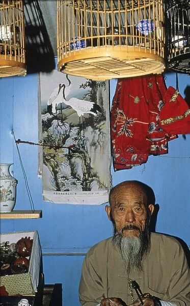 Bird trader in Beijing bird market China 1993. Siberian Rubythroat in cage hanging from ceiling