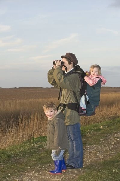 mother carrying toddler in backpack while bird watching along coastal path North
