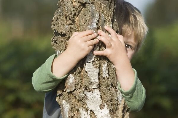 Toddler playing peek a boo behind tree