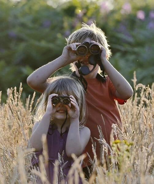 Young boy and girl ) brother and sister) bird watching in meadow in summer Norfolk