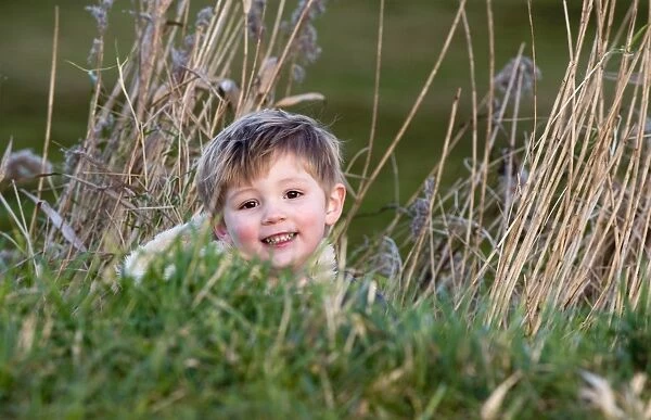 young boy playing hide and seek in reeds Norfolk winter