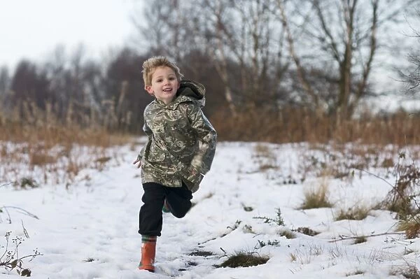 Young boy running through snow Norfolk winter