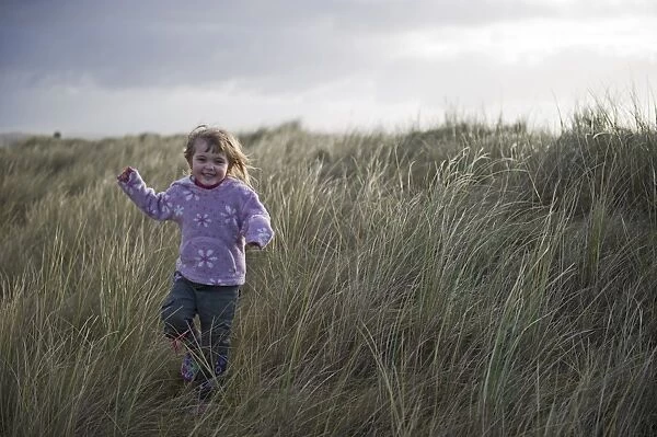Young girl playing in sand dunes Waxham Norfolk winter