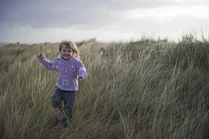 Framed Print : Young girl playing in sand dunes Waxham Norfolk winter