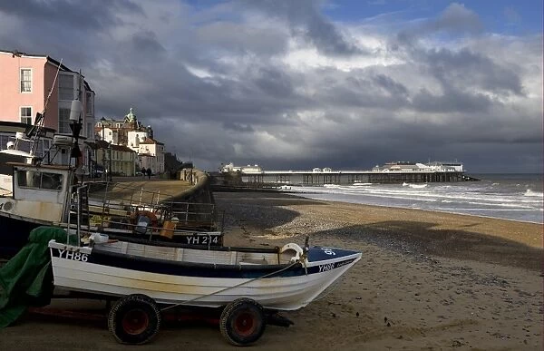 View of fishing boats, beach and pier of seaside town, with stormclouds overhead, Cromer Pier, Cromer, Norfolk