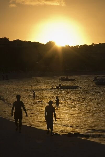 Antigua, Long Bay Beach, people in the water and walking along beach at sunset