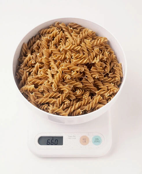 Bowl of wholewheat fusilli pasta being weighed on scales with liquid crystal display, view from above