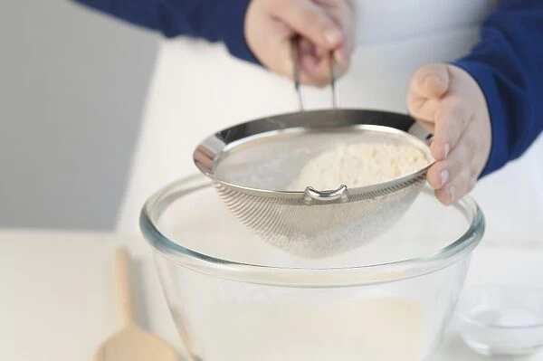 Person sieving flour into glass bowl