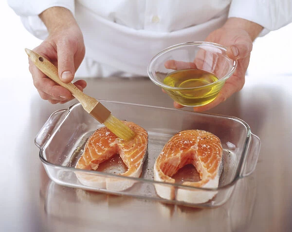 Two salmon steaks in a glass tray being brushed with oil, high angle view