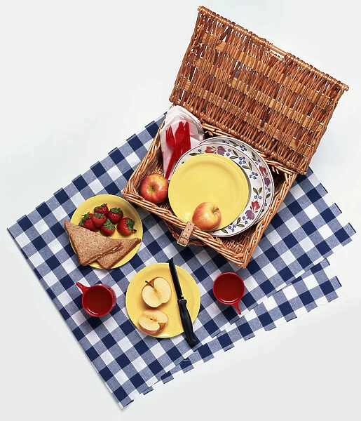 Wicker picnic hamper filled with sandwiches, fruit, plates and cutlery