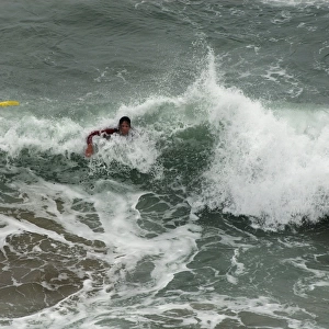 An RNLI lifeguard swimming through heavy surf at Perranporth