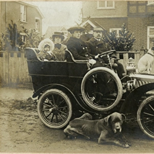 People in an early car with two dogs