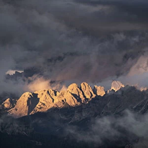 Light rays hitting Dolomites mountain peaks at sunset, surrounded by low clouds and mist, Cortina d Ampezzo, Dolomites, Veneto, Italy, Europe