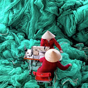 Vietnam, Cam Ranh, women mend green fishing nets using a sewing machine