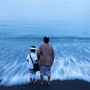 A Balinese Hindu woman hold her grandsons hand on a beach during Melasti