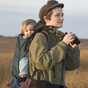 mother carrying toddler in backpack while bird watching along coastal path North