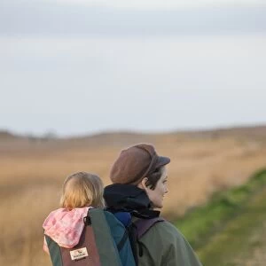 mother carrying toddler in backpack along coastal path North Norfolk winter