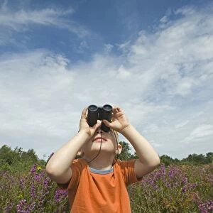Young boy looking through binoculars on heath Norfolk summer