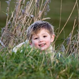 young boy playing hide and seek in reeds Norfolk winter