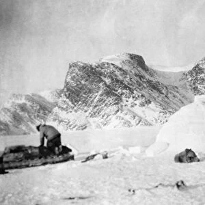 CANADA: ESKIMO IGLOO. An Eskimo man kneeling on his kayak next to his snow house