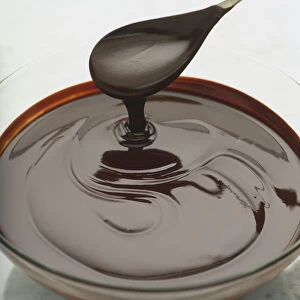 Dripping spoon being lifted up from bowl of dark chocolate sauce, close up
