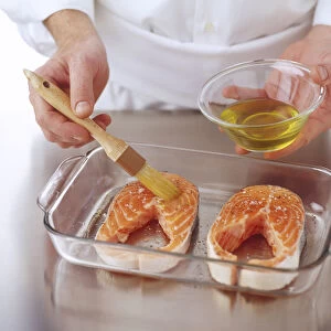Two salmon steaks in a glass tray being brushed with oil, high angle view