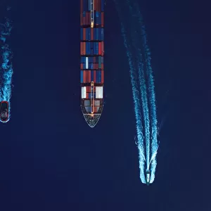 Aerial view of a cargo ship being guided by a tugboat and a pilot boat into the harbour