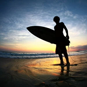 Surfer on beach at sunset