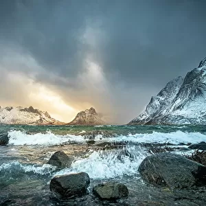 Winter storm clouds gathering along rocky shore surrounded by snow-covered mountains, Lofoten Island, Norway. March, 2023