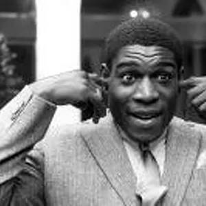Frank Bruno stands with his hands raised and his fingers in his ears