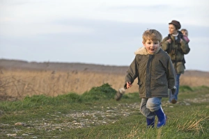 mother carrying toddler in backpack along coastal path North Norfolk winter
