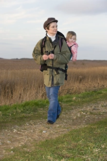 mother carrying toddler in backpack along coastal path North Norfolk winter