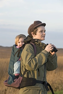 mother carrying toddler in backpack along coastal path North Norfolk winter