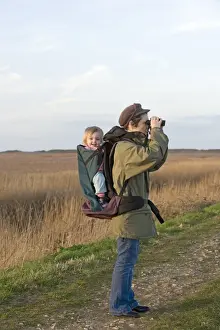 mother carrying toddler in backpack while bird watching along coastal path North