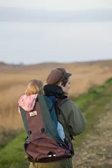 Mother Prints: mother carrying toddler in backpack along coastal path North Norfolk winter