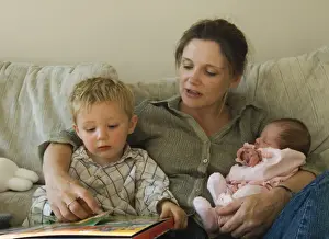 Images Dated 6th August 2006: Mother, toddler and new born girl reading childrens book on sofa at home Norfolk UK