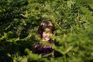 Young girl peeping from among bracken on heath in summer Norfolk Young girl peeping from among bracken on heath in summer Norfolk