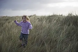 Children Prints: Young girl playing in sand dunes Waxham Norfolk winter